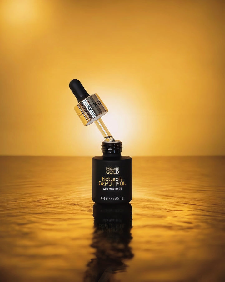 A bottle of Nature's Gold Naturally Beautiful with Manuka Oil with dropper out on top of water on a glowing yellow background